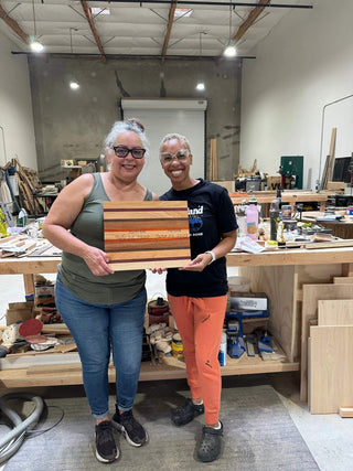 Two people holding a wooden panel in a workshop setting