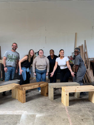 Group of people posing with wooden benches in a workshop setting