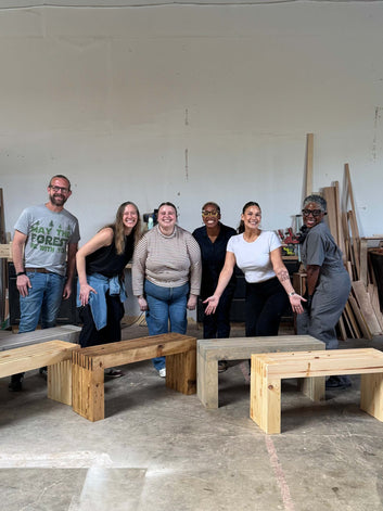 Group of people posing with wooden benches in a workshop setting