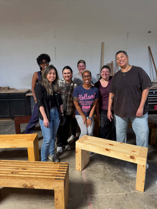 Group of people posing with wooden benches in a workshop.