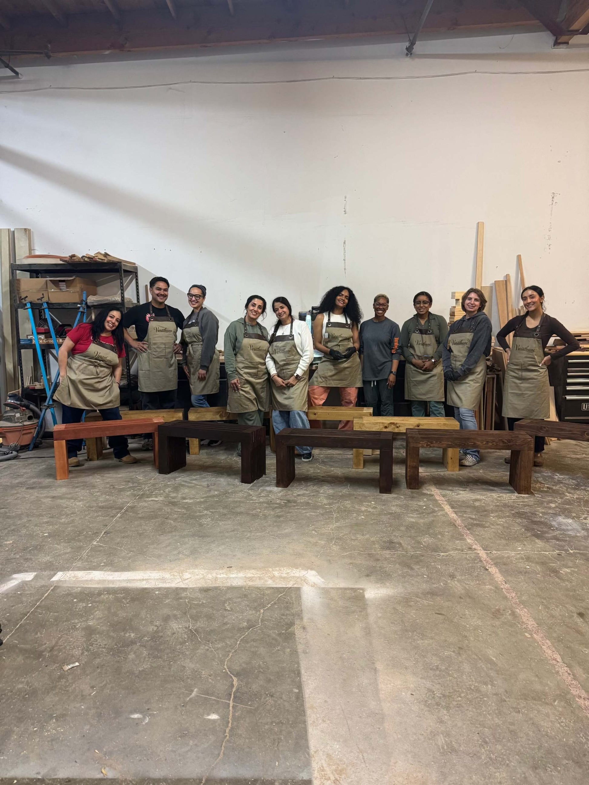 Group of people wearing aprons posing for a photo in a workshop setting.