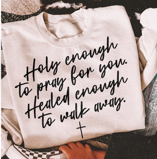 White sweatshirt with black text and a cross symbol, held by a person.