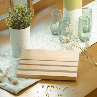 Wooden cutting board on a table with a plant and glasses in the background