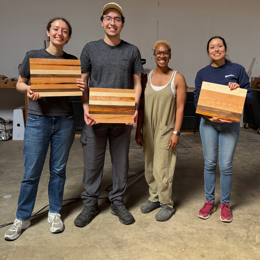 Four people holding wooden cutting boards in a workshop setting