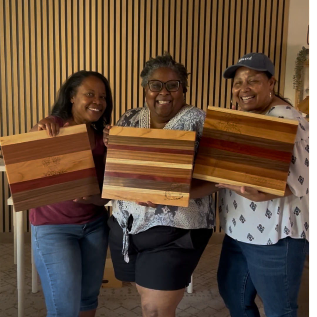 Three women holding wooden cutting boards indoors